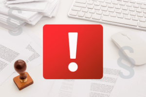 Czerwony wykrzyknik, z tyłu klawiatura , myszka , pieczątka oraz dokumenty.